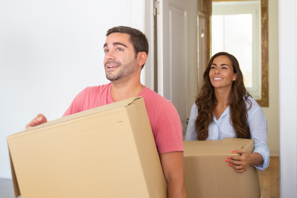 Joyful young Latin couple coming in their new apartment with carton boxes.