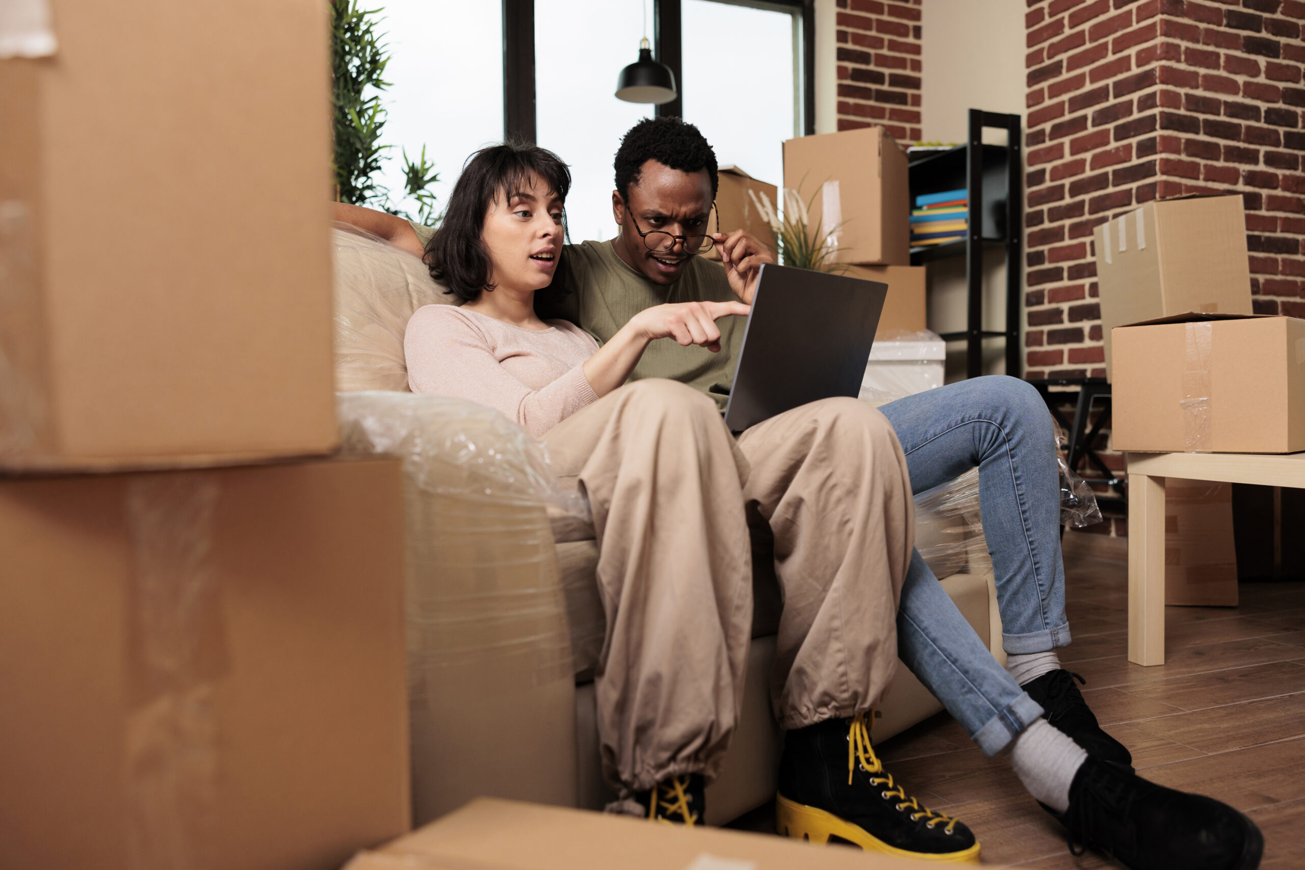 Diverse man and woman doing online shopping to buy furniture, browsing internet website for home decor inspiration. Moving in rented apartment property together for relationship event.