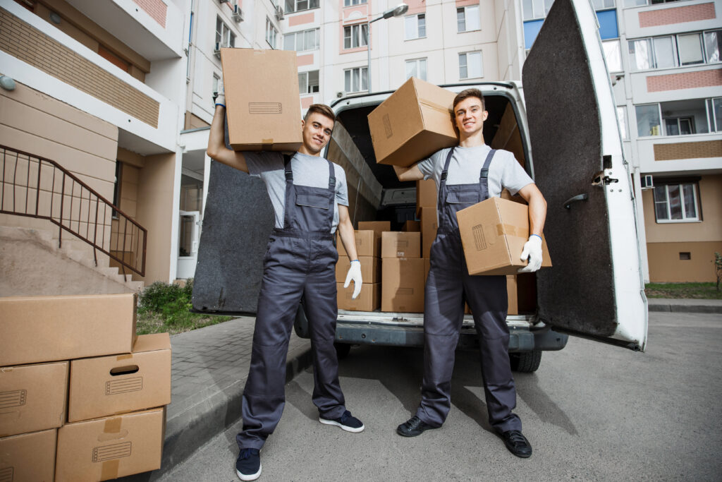 Two professional movers in uniforms holding boxes in front of a moving van, ready for a house move.