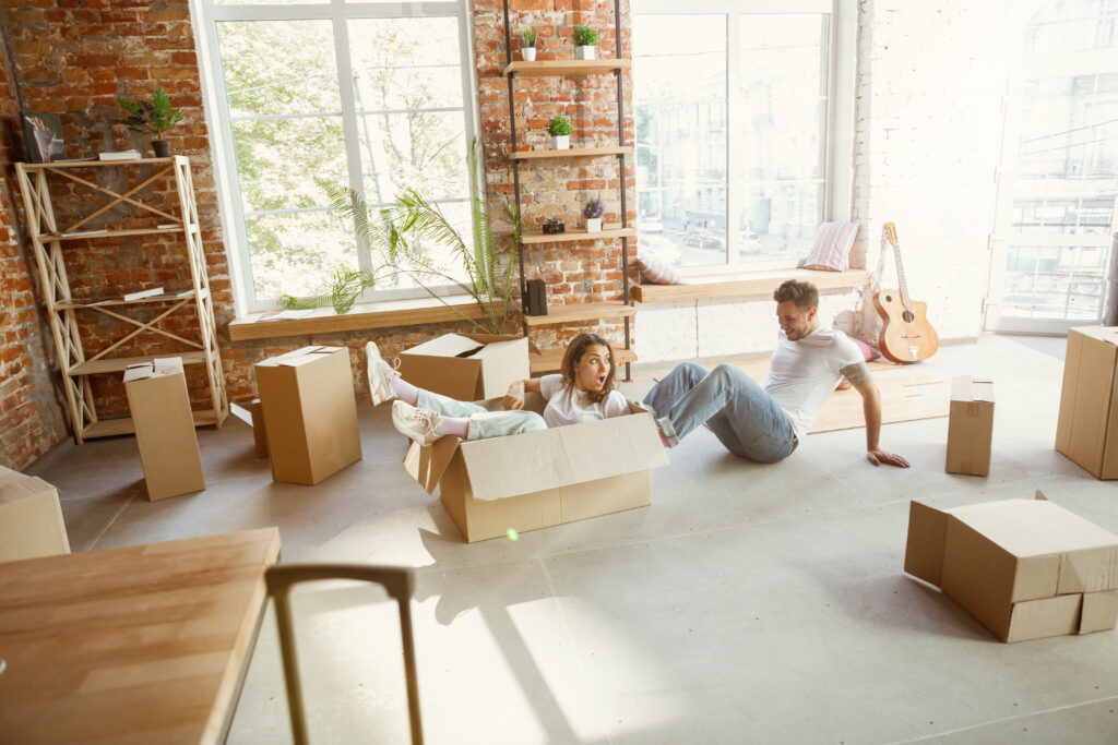 Young couple moved to a new house or apartment. Having fun with cardboard boxes, relaxing after cleaning and unpacking at moved day.